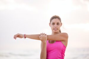 Woman in pink exercise gear stretching her arm.