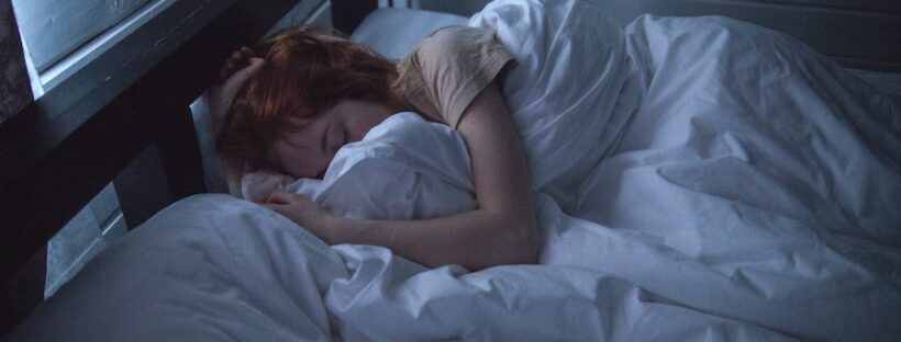 Woman with red hair sleeping in bed with white sheets.